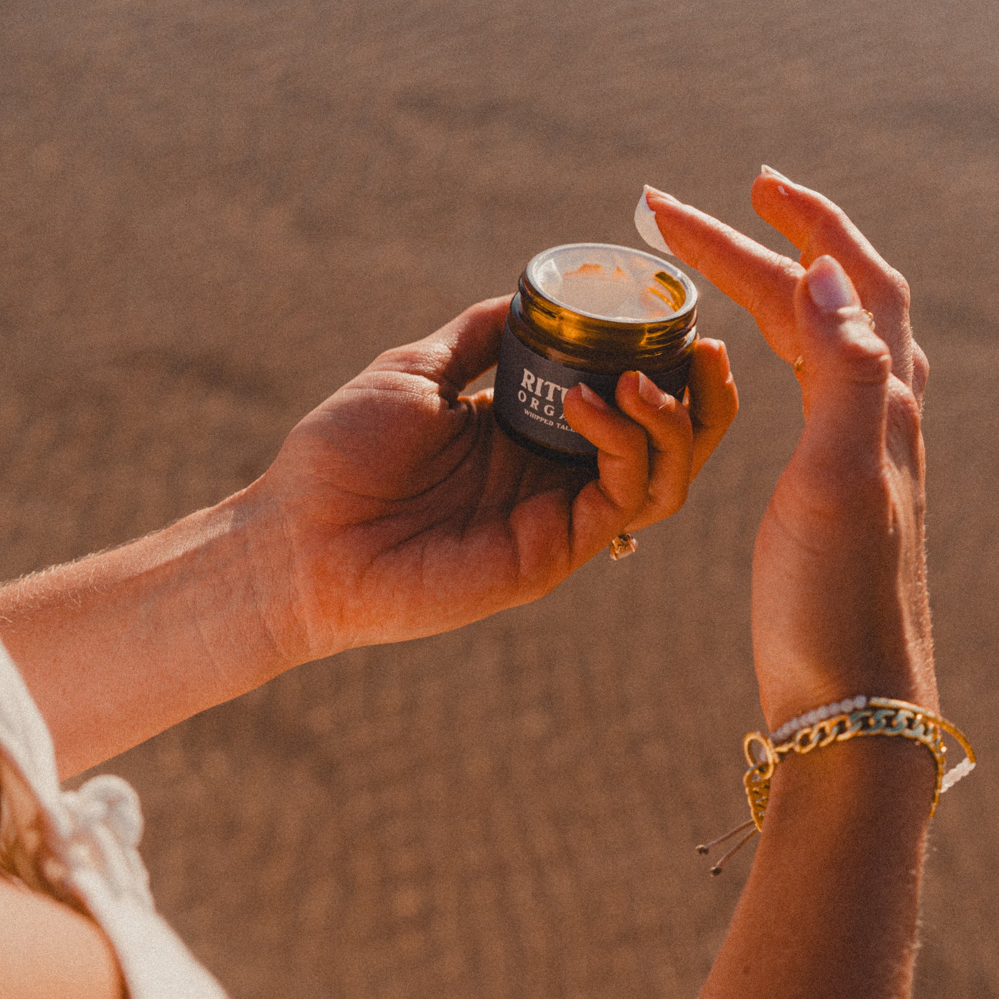Person holding a jar of Ritual Organics Whipped Tallow with Zinc on a beach