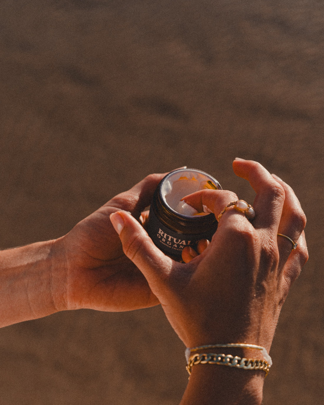 Hands opening a jar of Ritual Organics Whipped Tallow Sun Balm at golden hour